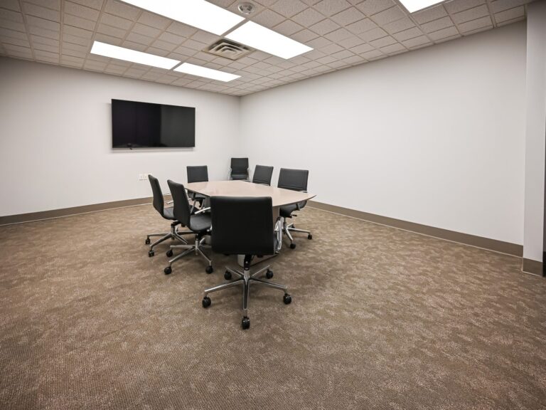 Renovated conference room at a Troy title office with a round table, black task chairs, carpet tile and a wall-mounted TV