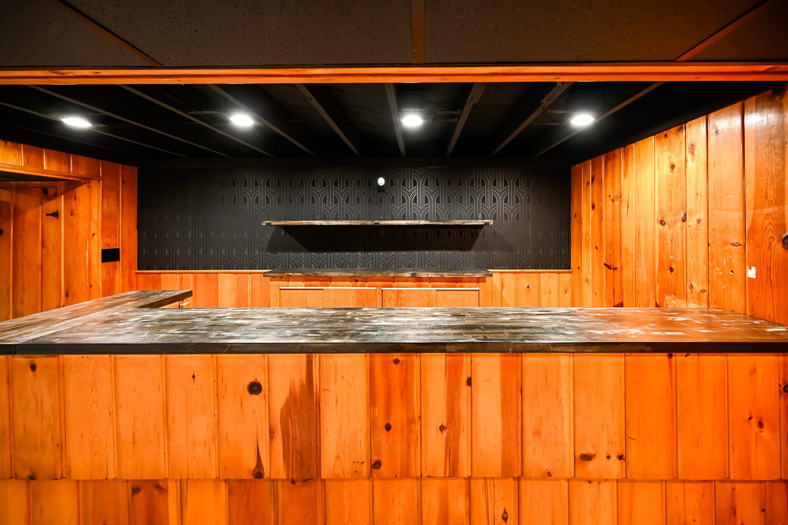 Black art deco accent wall behind a bar with a dark stained shelf in a finished Ypsilanti basement