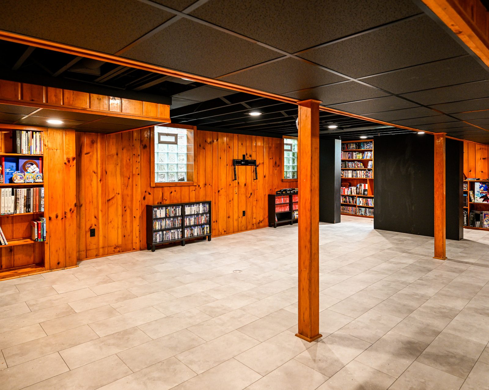 Finished Ypsilanti basement with built-in shelving displaying a game collection against knotty pine walls