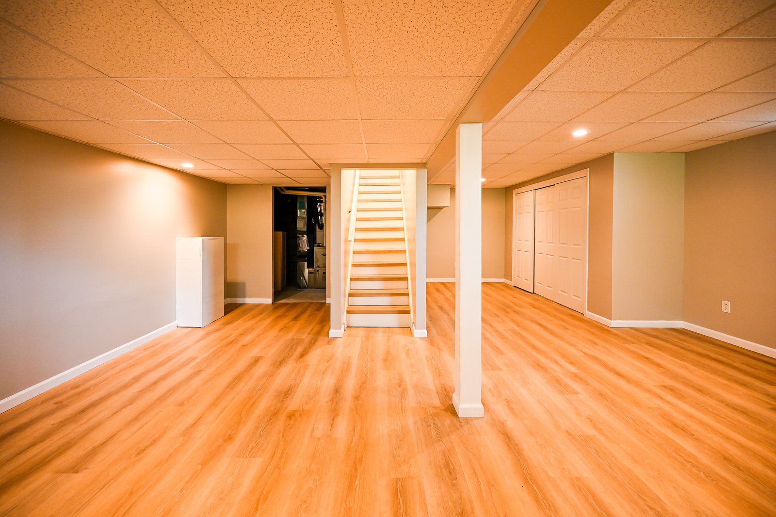 Open refinished basement room in Ypsilanti with stairs, closet wall and warm plank flooring