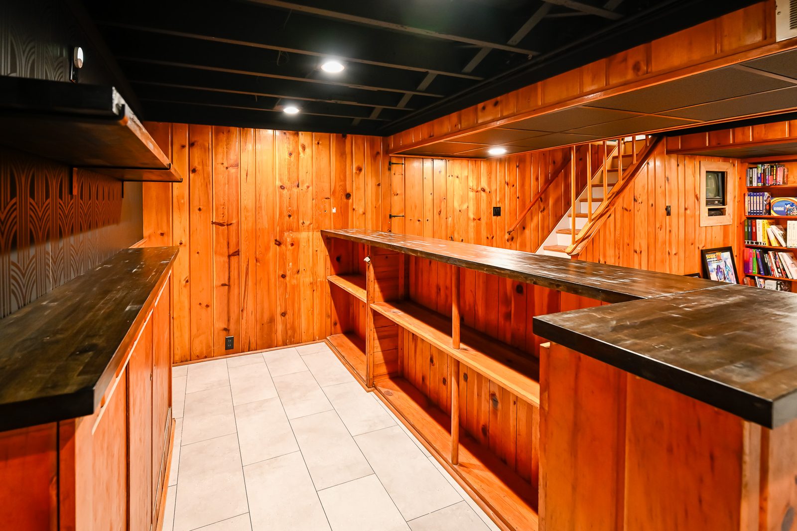 Built-in bar with dark stained top and open shelving beside finished basement stairs in Ypsilanti