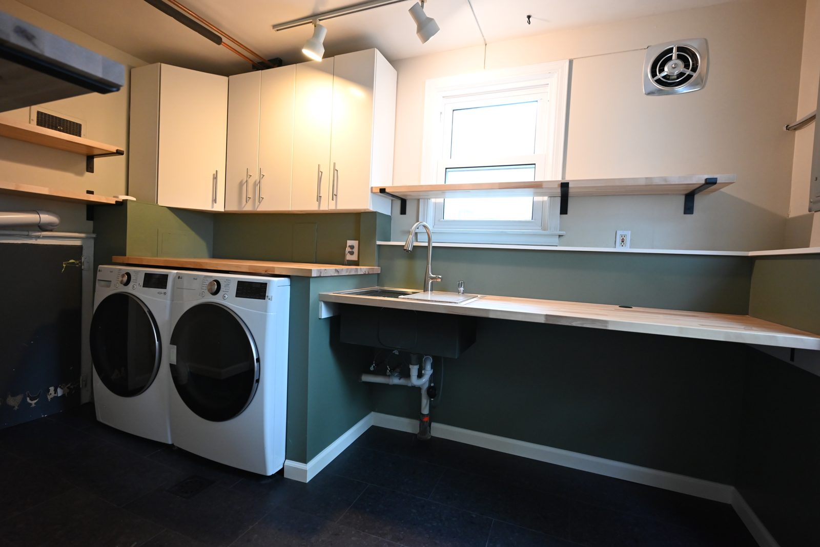 Wide view of the remodeled Ypsilanti laundry room with sink, washer, dryer and open shelving