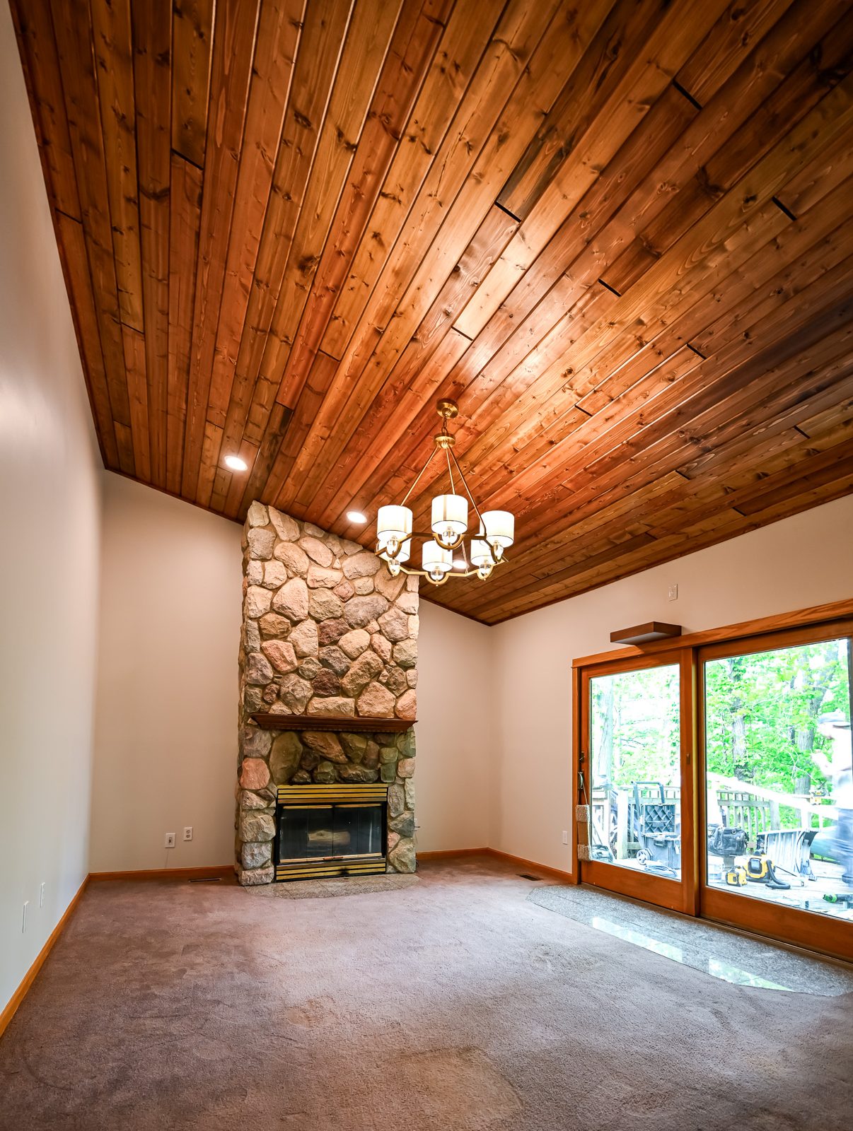 Full view of the remodeled Ypsilanti living room with pine ceiling, stone fireplace and sliding door