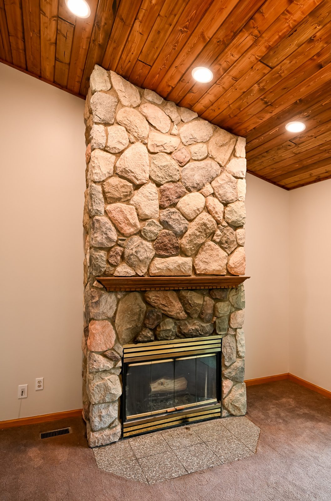 Stone chimney rising into the new knotty pine ceiling with a recessed light in Ypsilanti