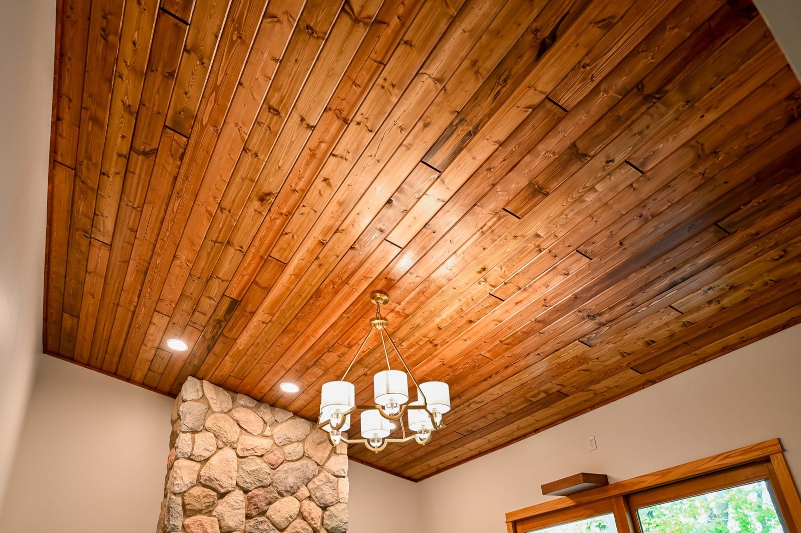 Vaulted knotty pine ceiling with a chandelier and stone chimney in a remodeled Ypsilanti living room