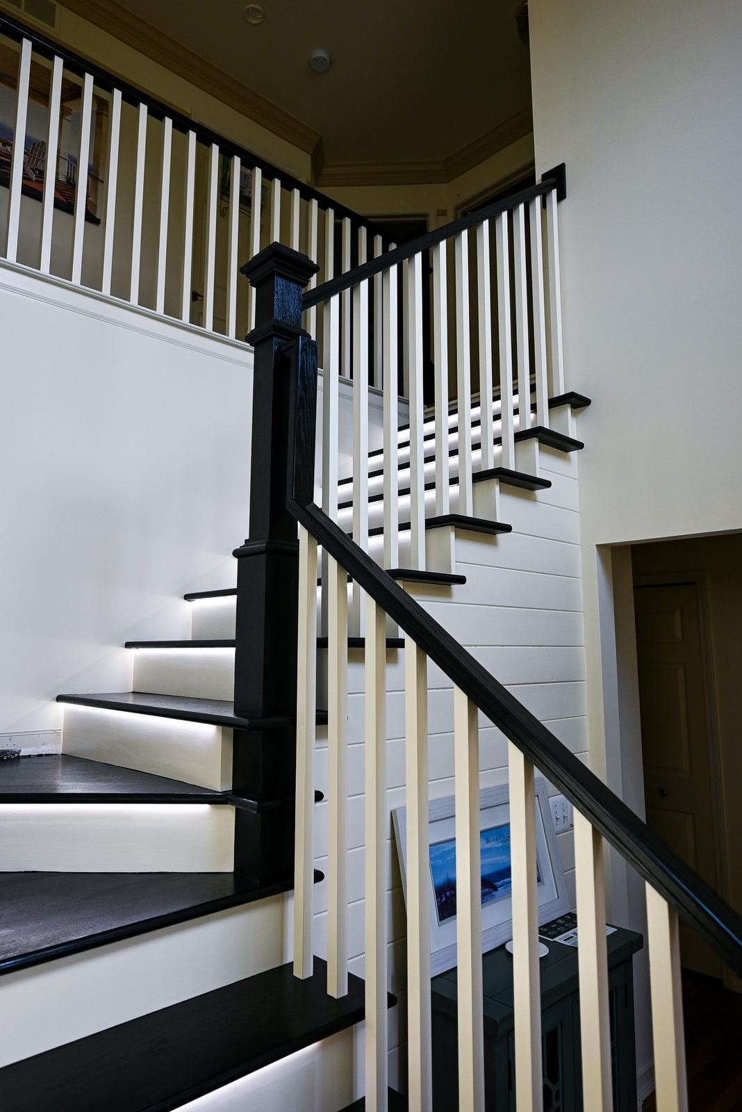 Staircase landing with white shiplap behind the upper flight, a black newel post and lighted treads below