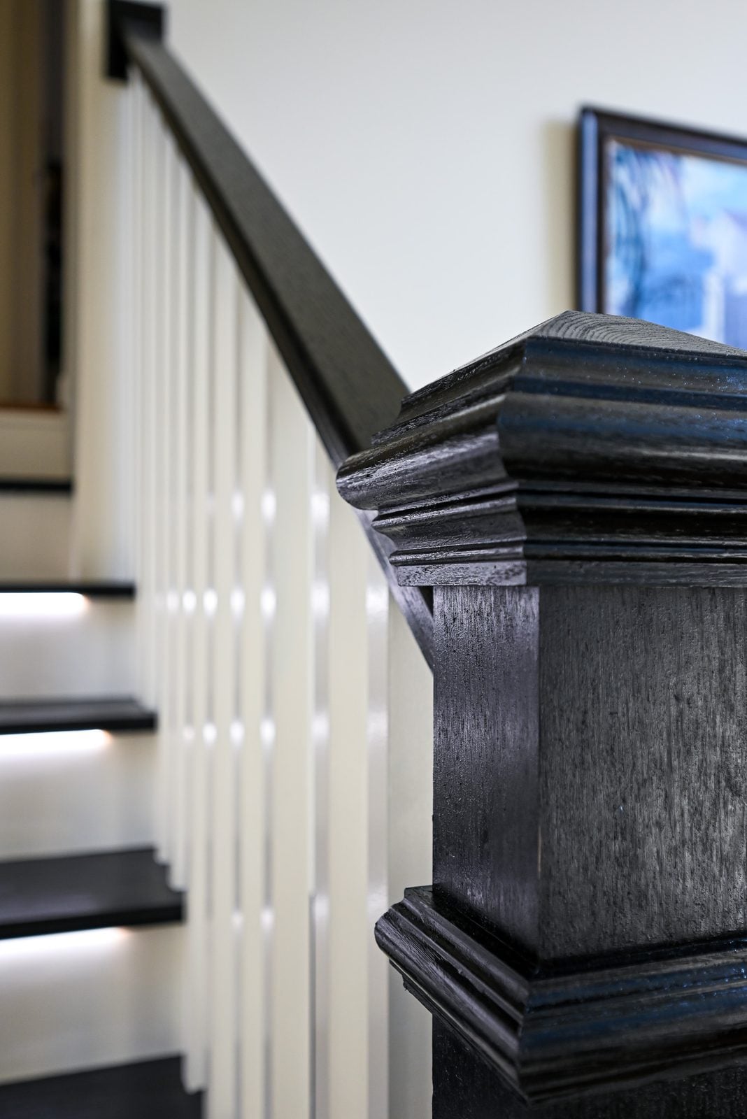 Close view of a black stained newel post cap with layered molding, oak grain visible through the finish