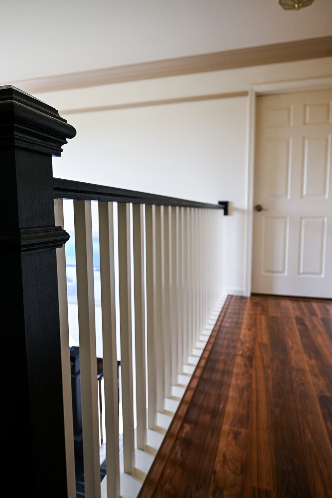 Upper hallway balustrade with black handrail and newel above a reddish brown plank floor