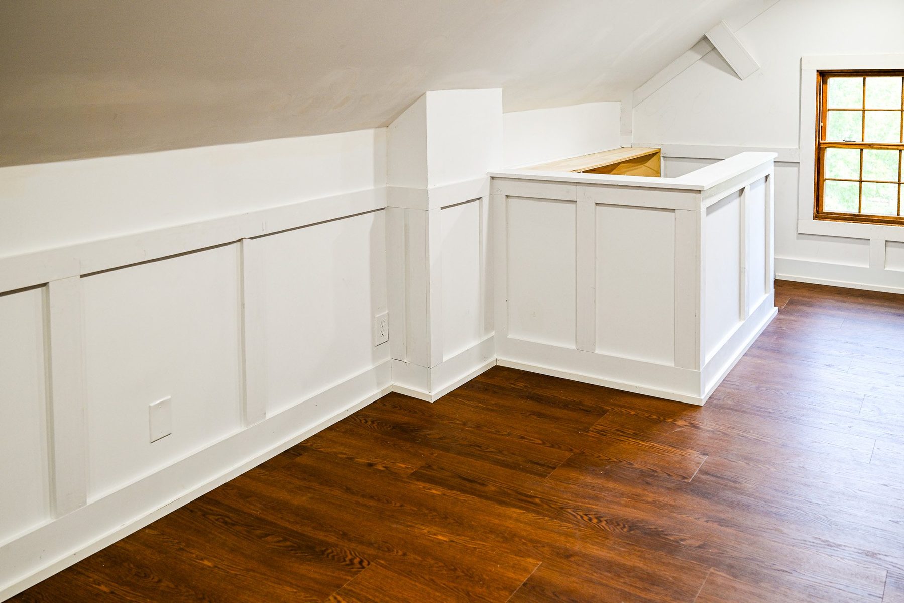 Attic knee walls finished in white panel wainscoting with a built-in return and hardwood floor