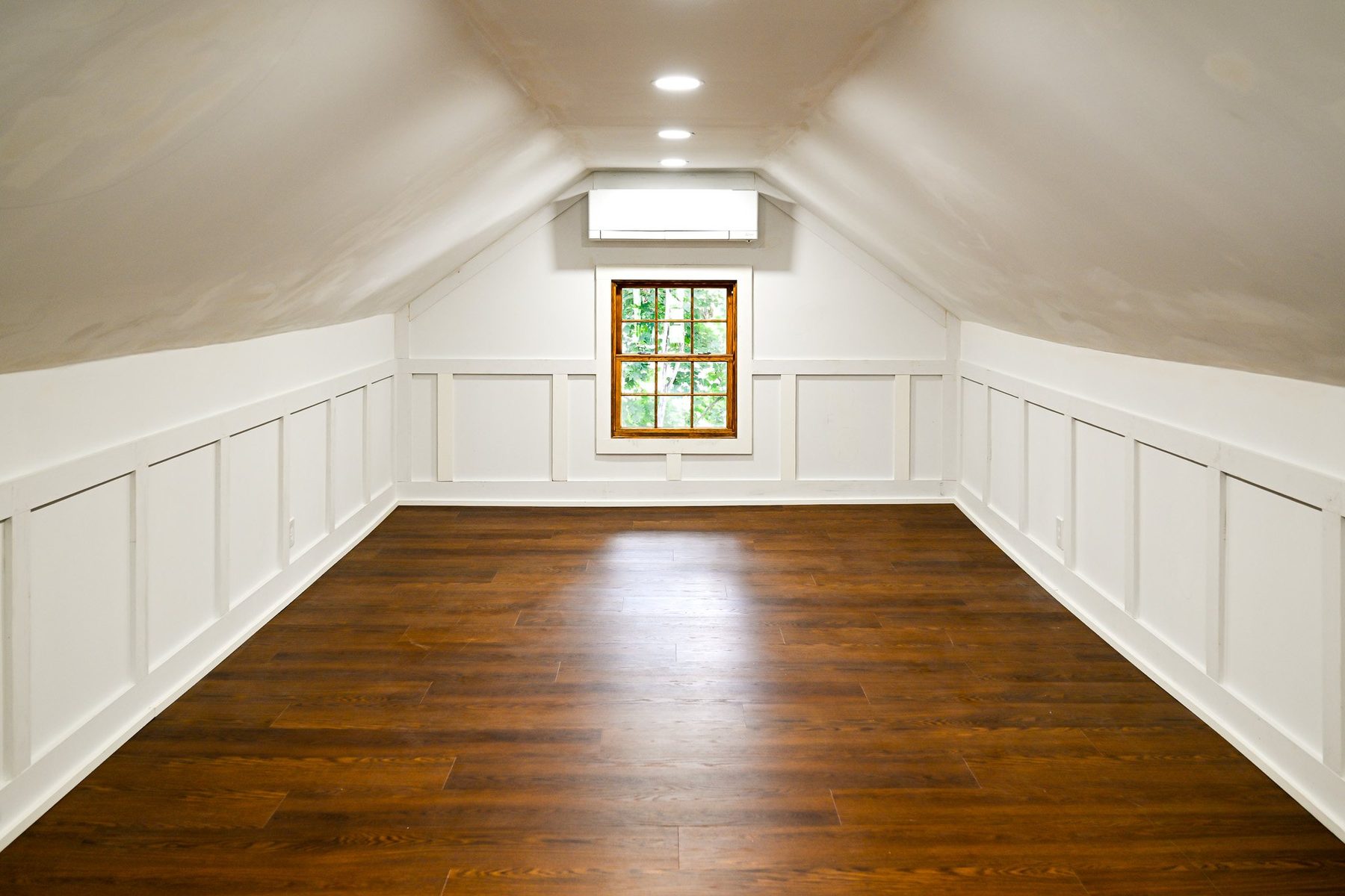 Finished attic room with a ductless mini-split on the end wall, recessed light and white wainscoted knee walls