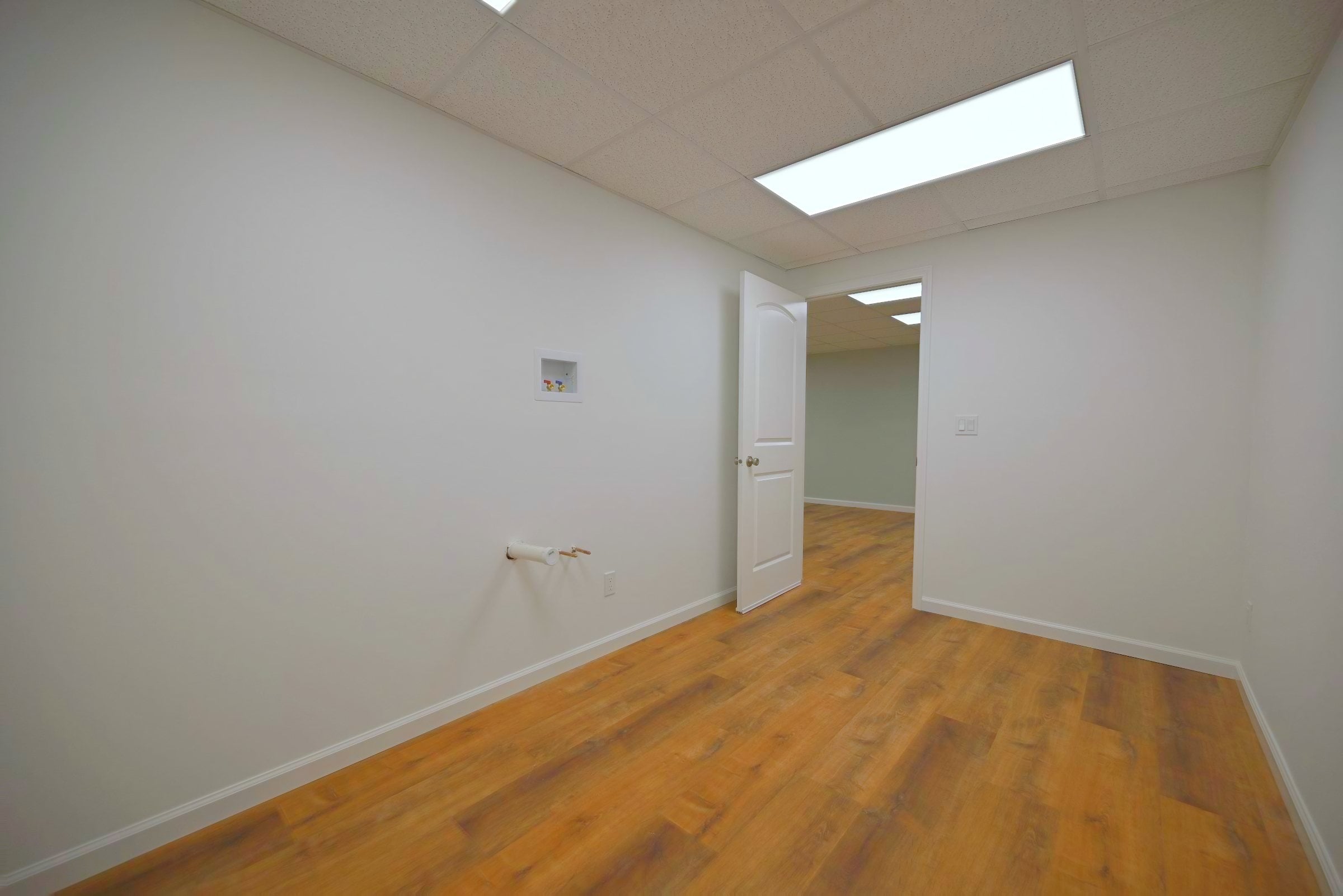 Basement darkroom with pale grey walls, a recessed supply box raised high on the wall, a capped drain stub with a shut off valve below it and a door open to the hallway
