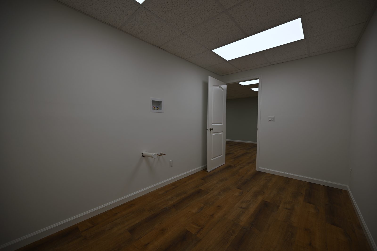 Basement darkroom with pale grey walls, a recessed supply box raised high on the wall, a capped drain stub with a shut off valve below it and a door open to the hallway