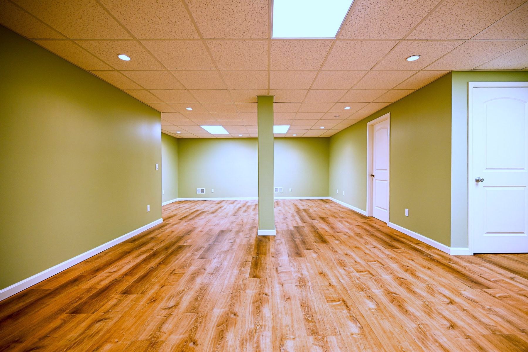 Long view of a finished basement rec room in Ann Arbor with a wrapped structural post, sage green walls and warm oak luxury vinyl plank floor