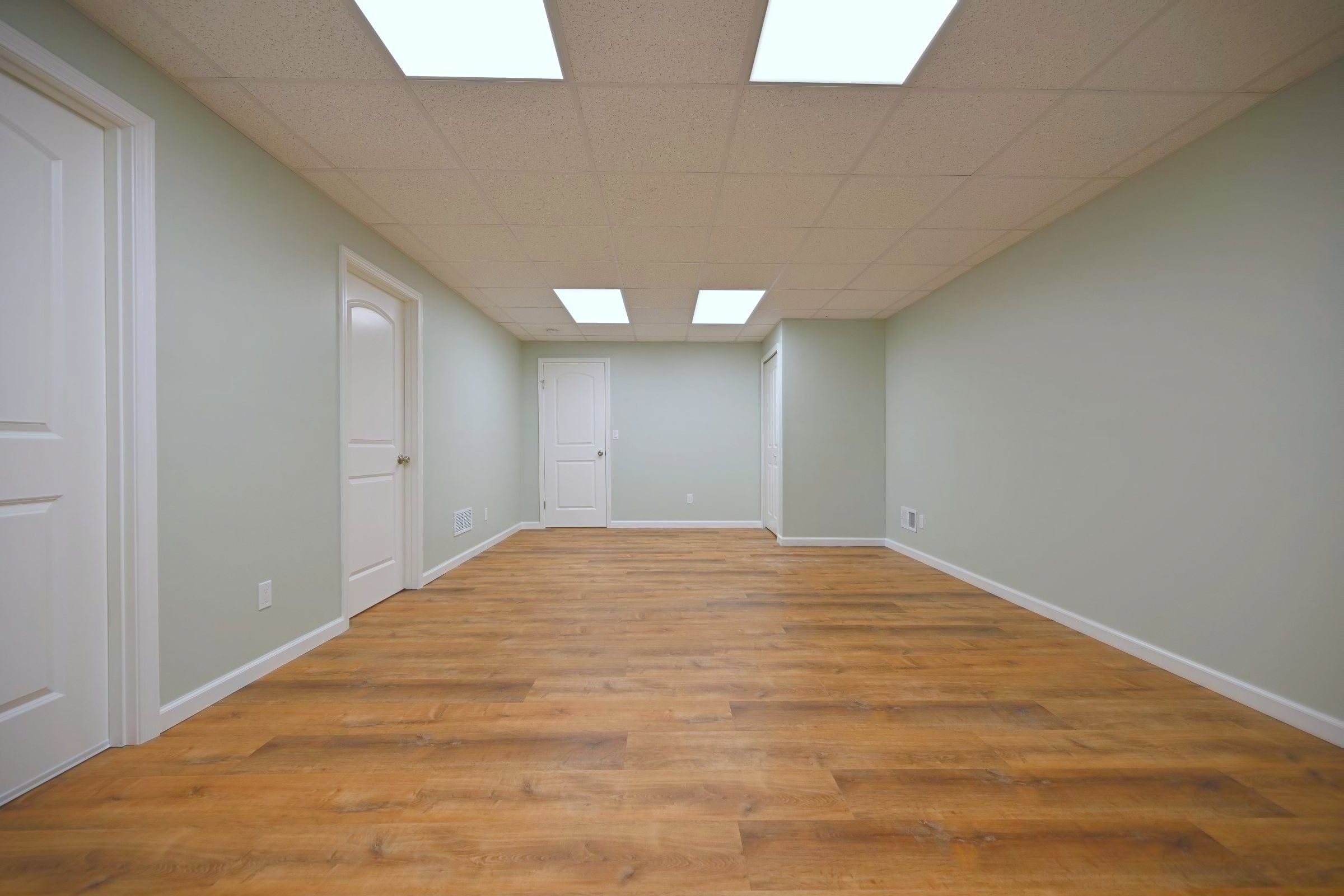 Second finished basement room painted a pale grey green with a small window, two panel doors and LED flat panels in the drop ceiling