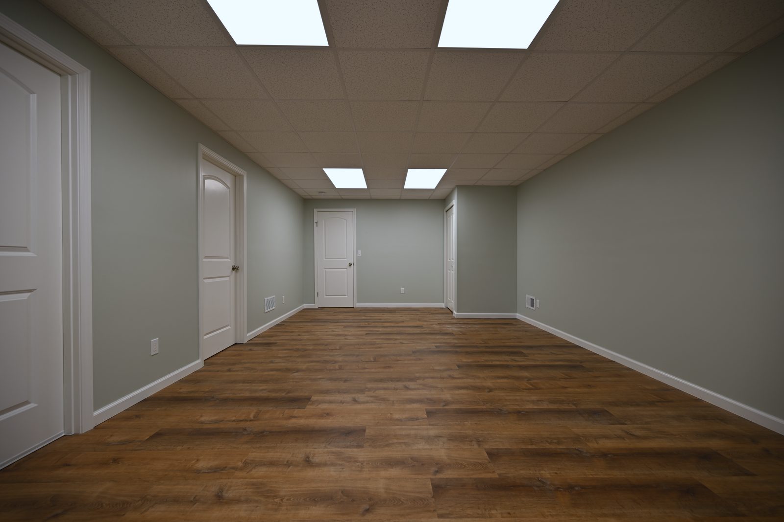 Second finished basement room painted a pale grey green with a small window, two panel doors and LED flat panels in the drop ceiling