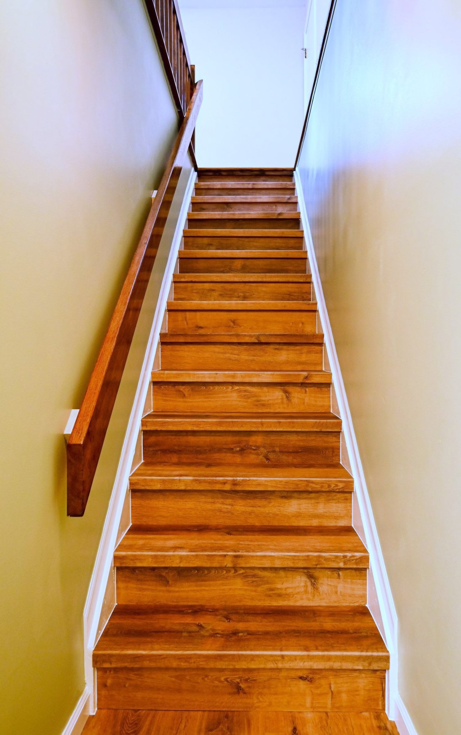 Basement stairway with luxury vinyl plank run over every tread, painted white risers and skirt board and a wood handrail