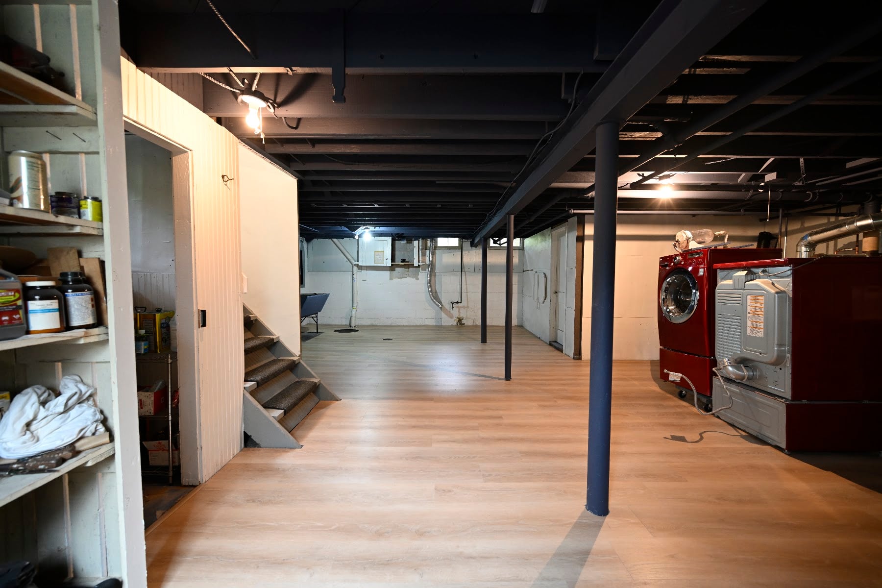 Basement laundry area beside the stairs with plank flooring running through to the far wall