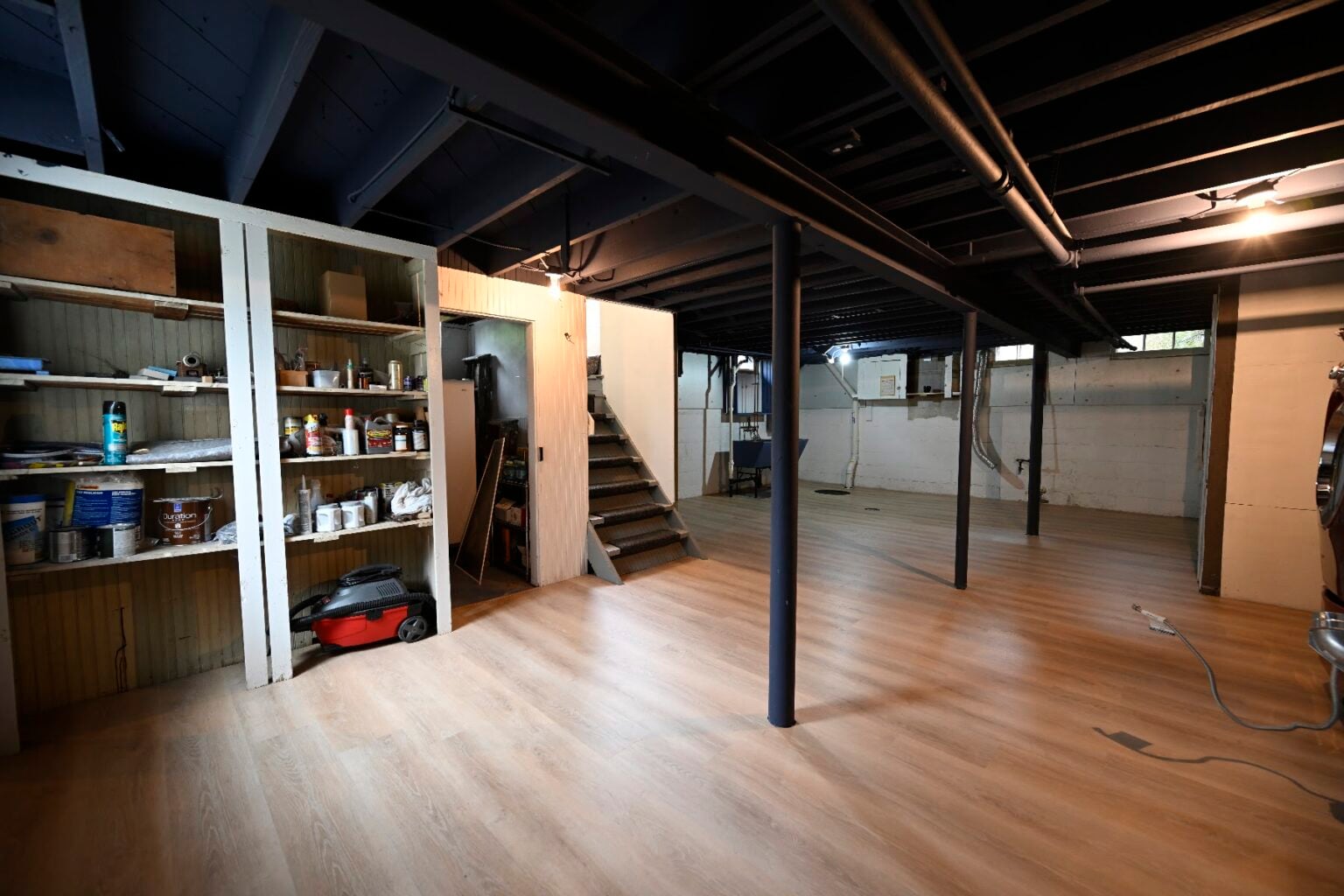 Finished Ann Arbor basement with a light plank floor, black sprayed ceiling and original built-in wood shelving