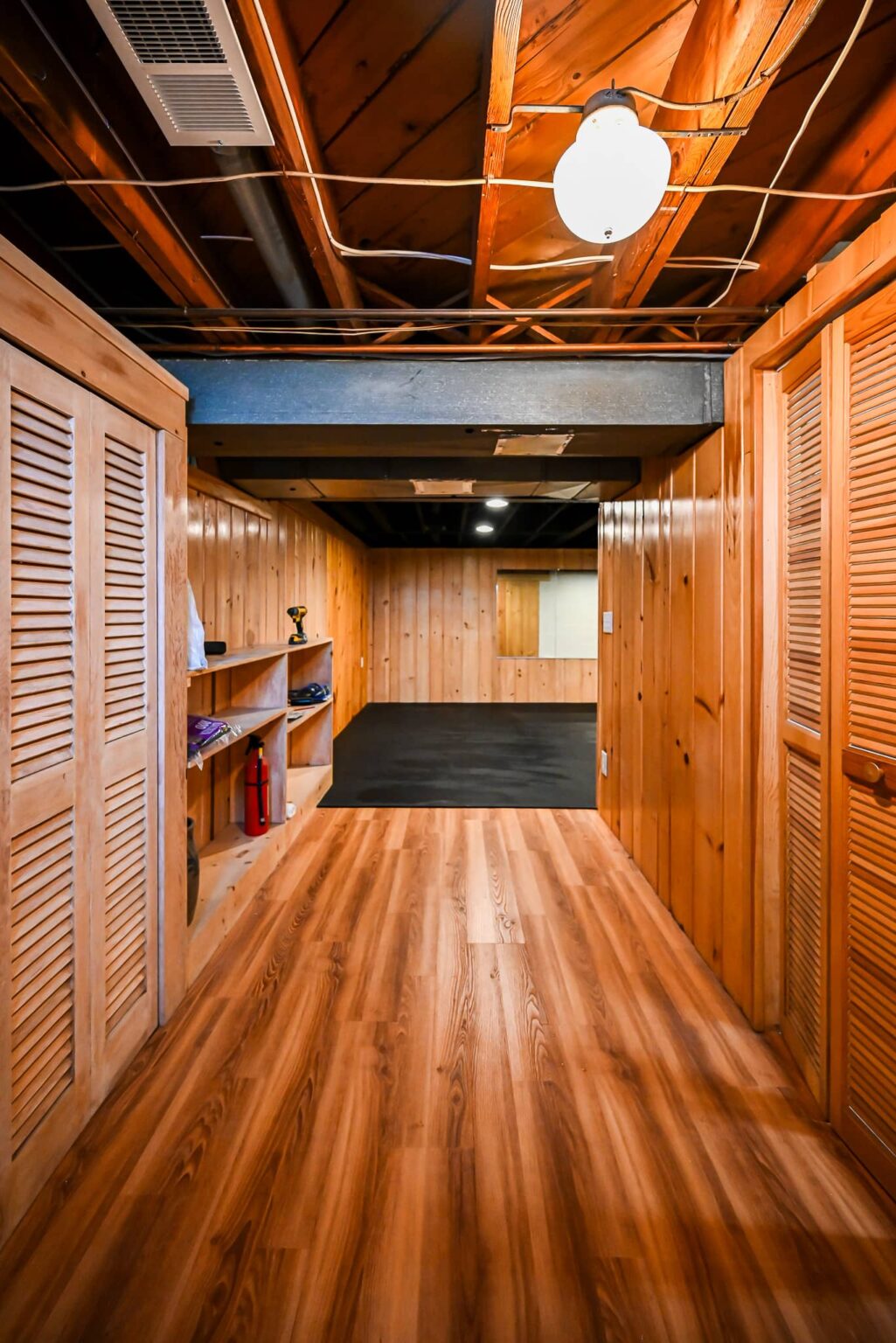 Basement walkway with knotty pine walls, louvered closet doors and new vinyl plank flooring leading to the gym