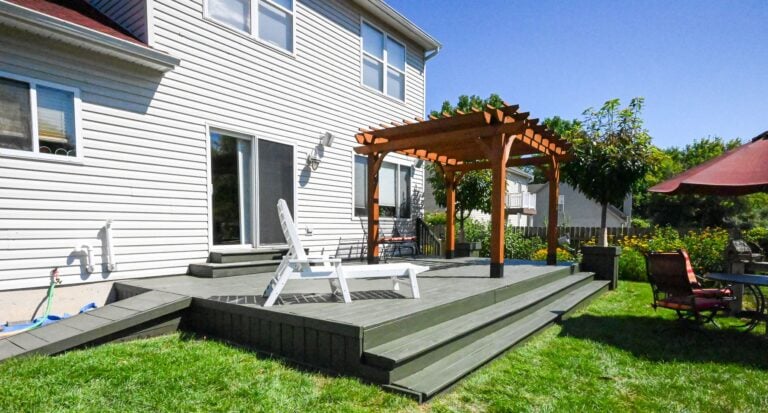 Refinished wood deck in Ann Arbor with wide stained steps, a rebuilt ramp along the house and a cedar pergola