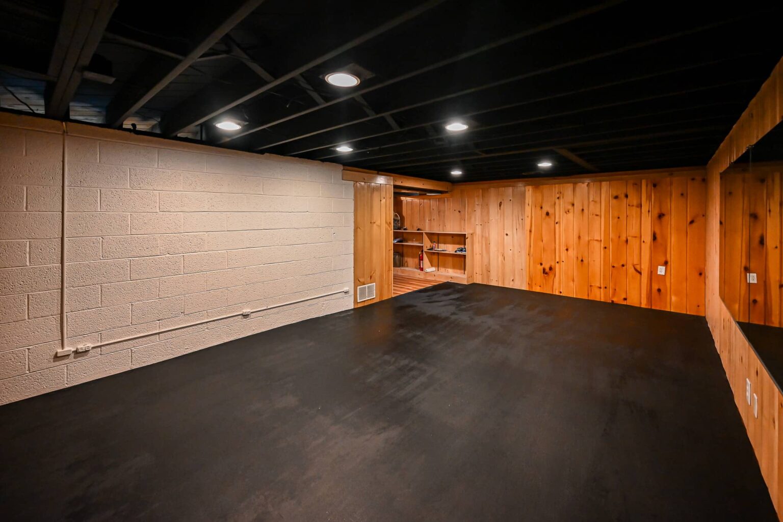 Finished basement home gym in Ann Arbor with a matte black sprayed ceiling, recessed LED lights, black rubber mats and painted block walls