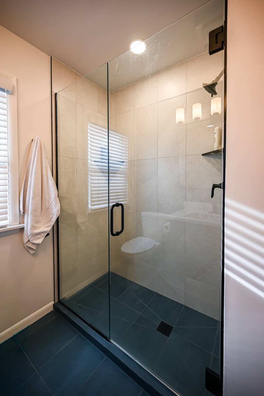 Walk-in shower with a frameless glass panel, matte black hardware, cream porcelain wall tile and a charcoal tile floor