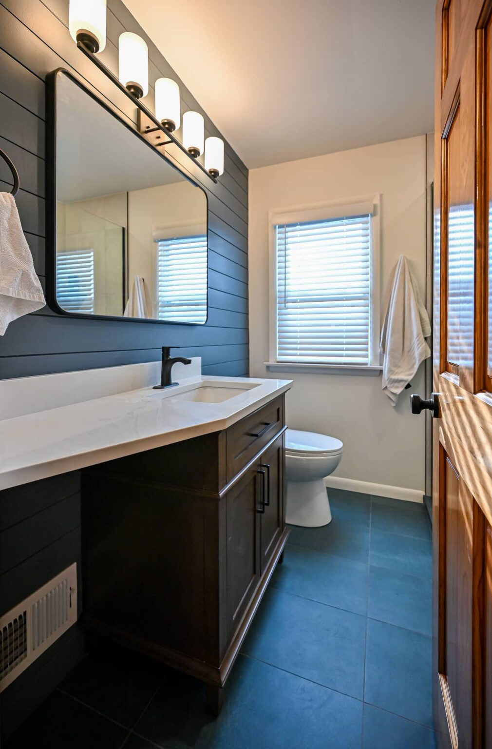 Remodeled primary bathroom in Ann Arbor with a navy shiplap wall, dark wood vanity, white quartz top and charcoal tile floor