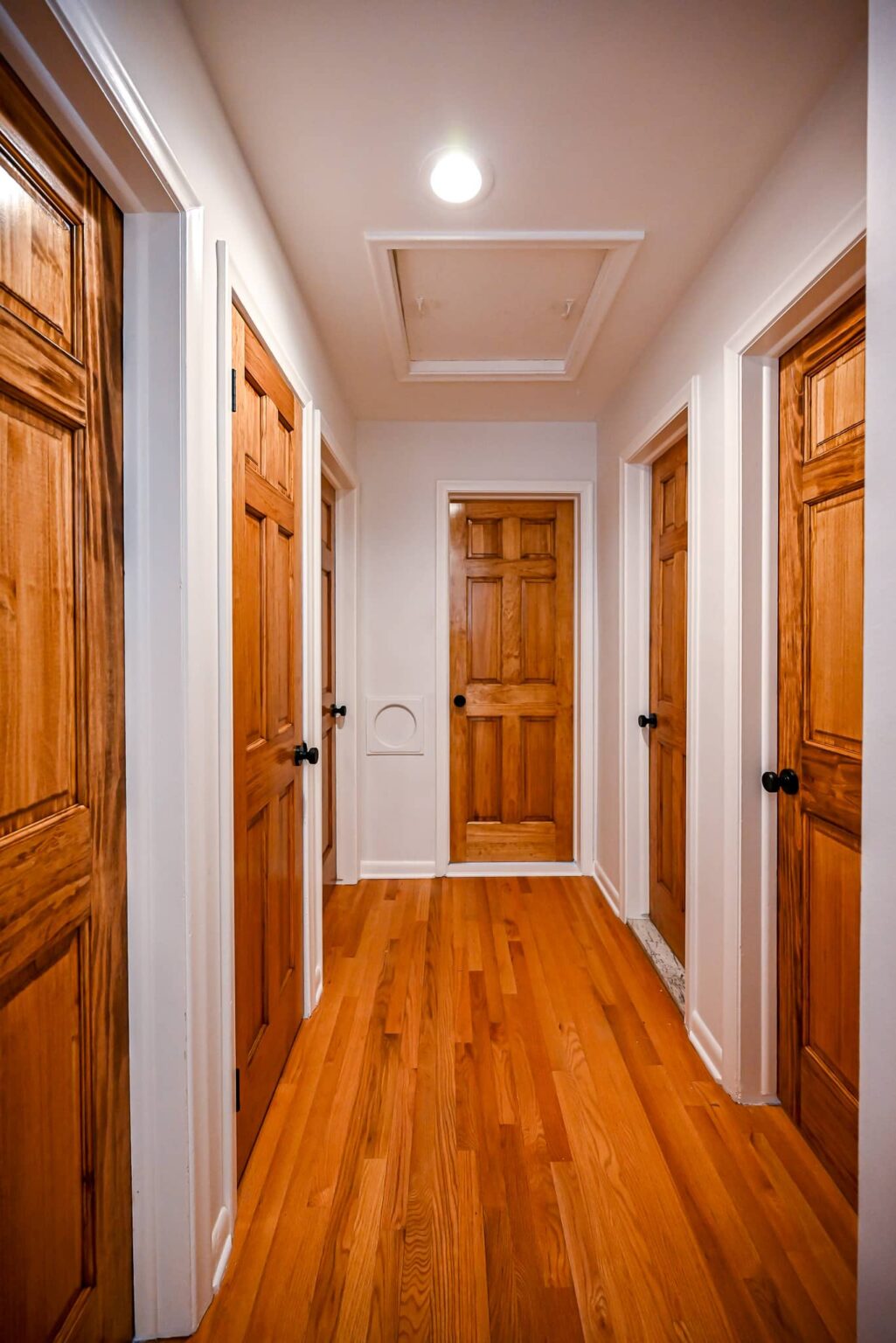 Hallway with warm wood six-panel doors, hardwood flooring and a recessed ceiling light