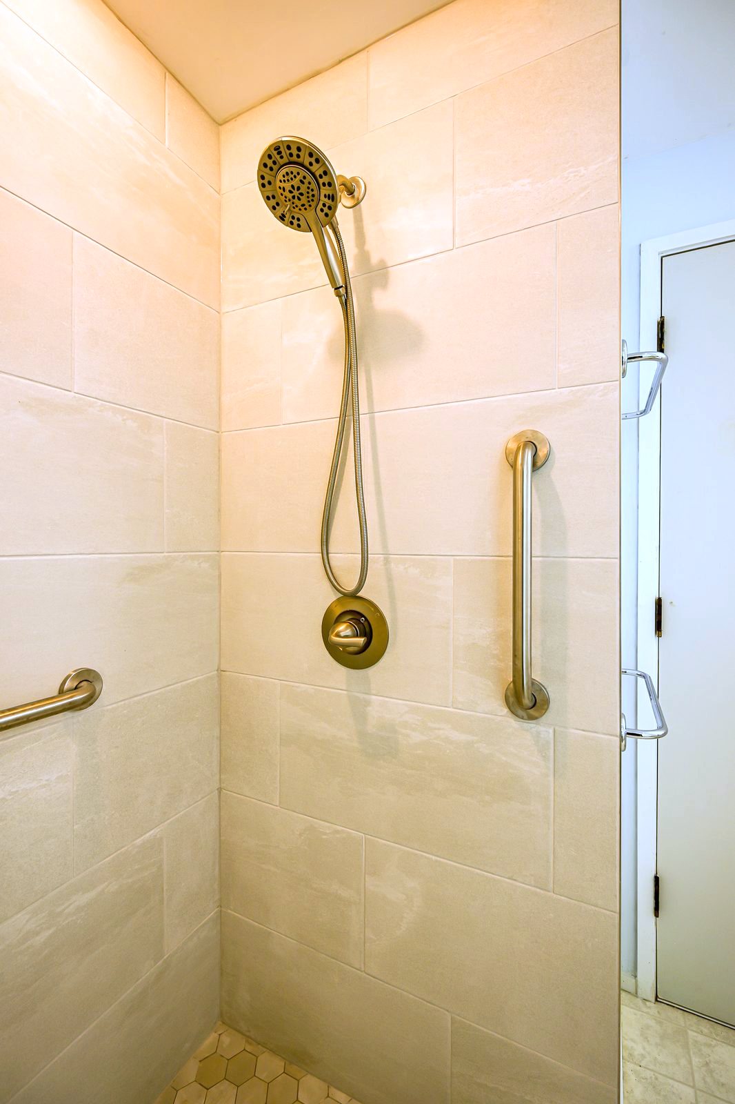 Handheld shower head on a slide bar with grab bars against large-format tile in Ann Arbor