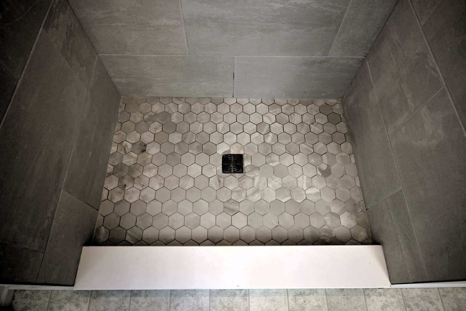 Hexagon mosaic shower floor sloped to a center drain behind a low curb in Ann Arbor