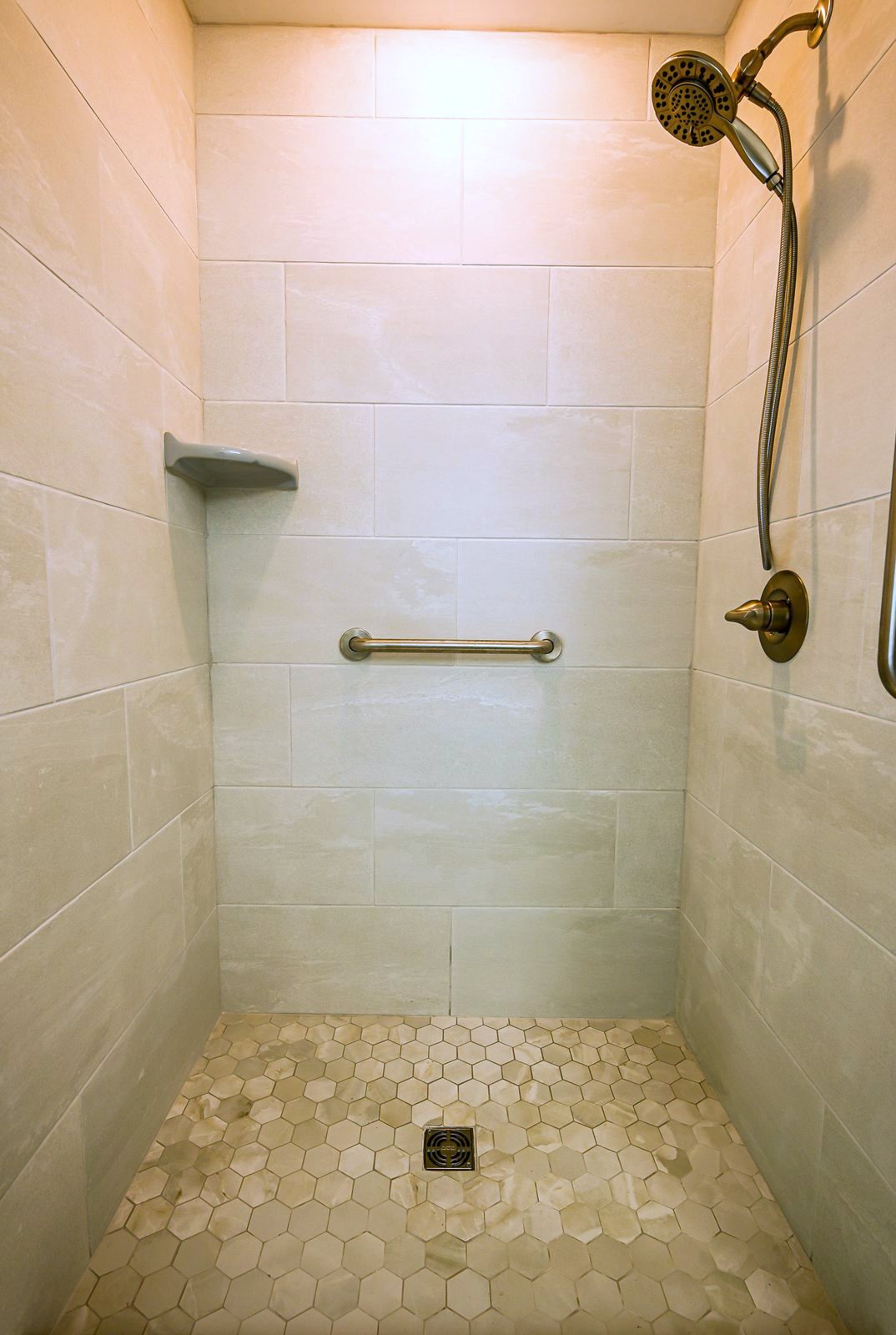 Walk-in shower interior with large-format tile walls, a corner shelf and a hexagon tile floor