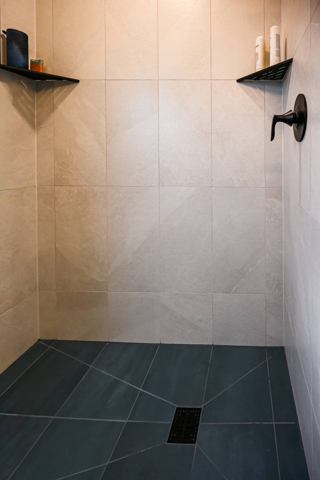Shower floor in charcoal porcelain tile with a square matte black drain and cream wall tile