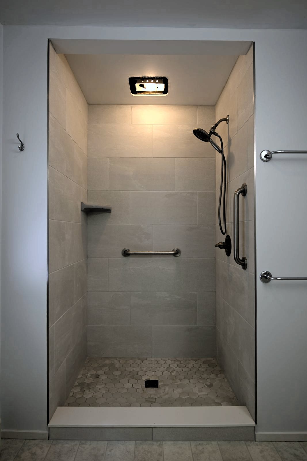 Tiled walk-in shower in the downstairs bathroom of an Ann Arbor home with grab bars and a hexagon mosaic floor
