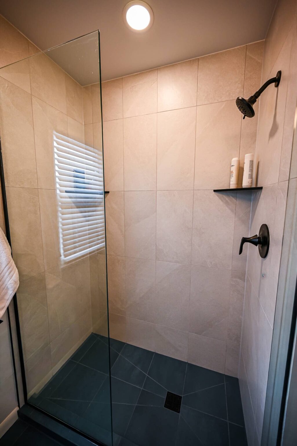 Walk-in shower with cream porcelain wall tile, a matte black rain head and corner shelves