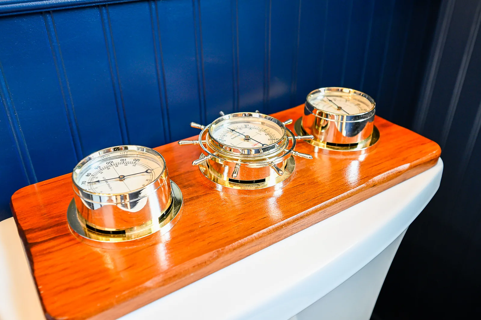 Brass ship barometer, thermometer and hygrometer mounted on a varnished wood board atop a toilet tank