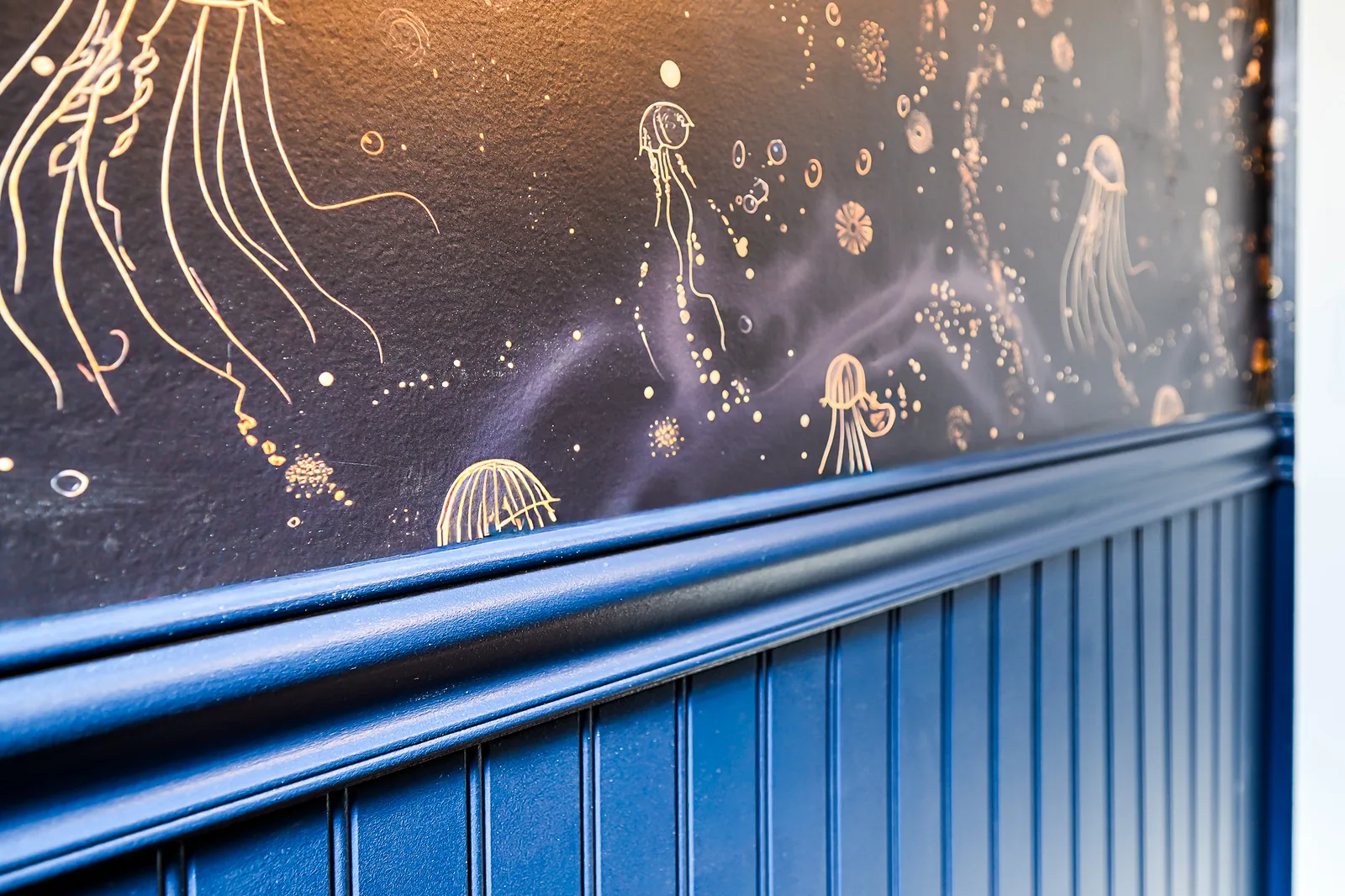 Close-up of gold line-drawn jellyfish wallpaper meeting a navy chair rail and beadboard