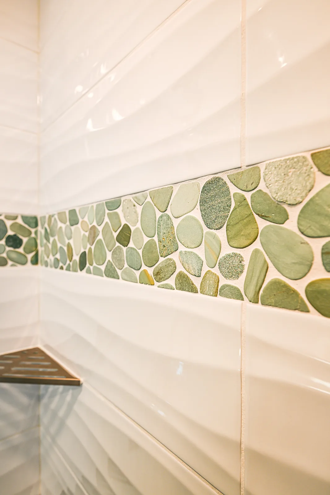 Close-up of a green river pebble accent band set between glossy white wave-pattern wall tiles