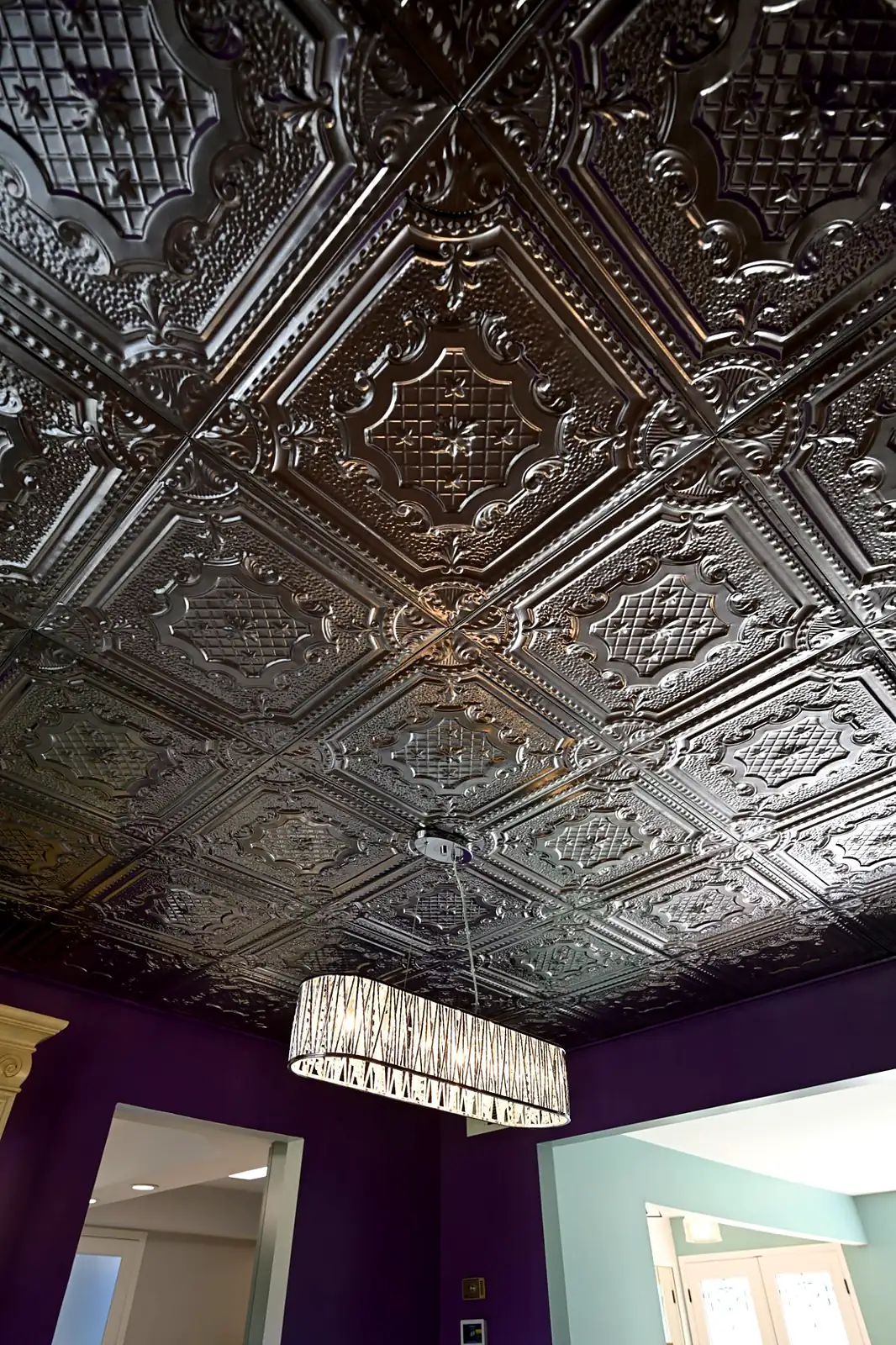 Looking up at a pressed metal ceiling with a linear crystal chandelier above a purple dining room