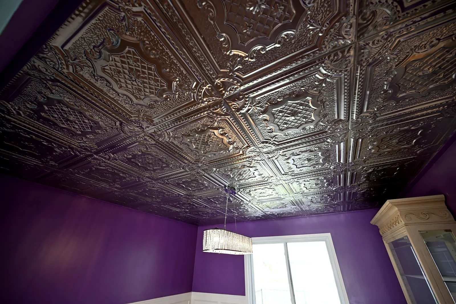 Dining room with an ornate pressed metal ceiling, deep purple walls, white wainscoting and a crystal drum chandelier