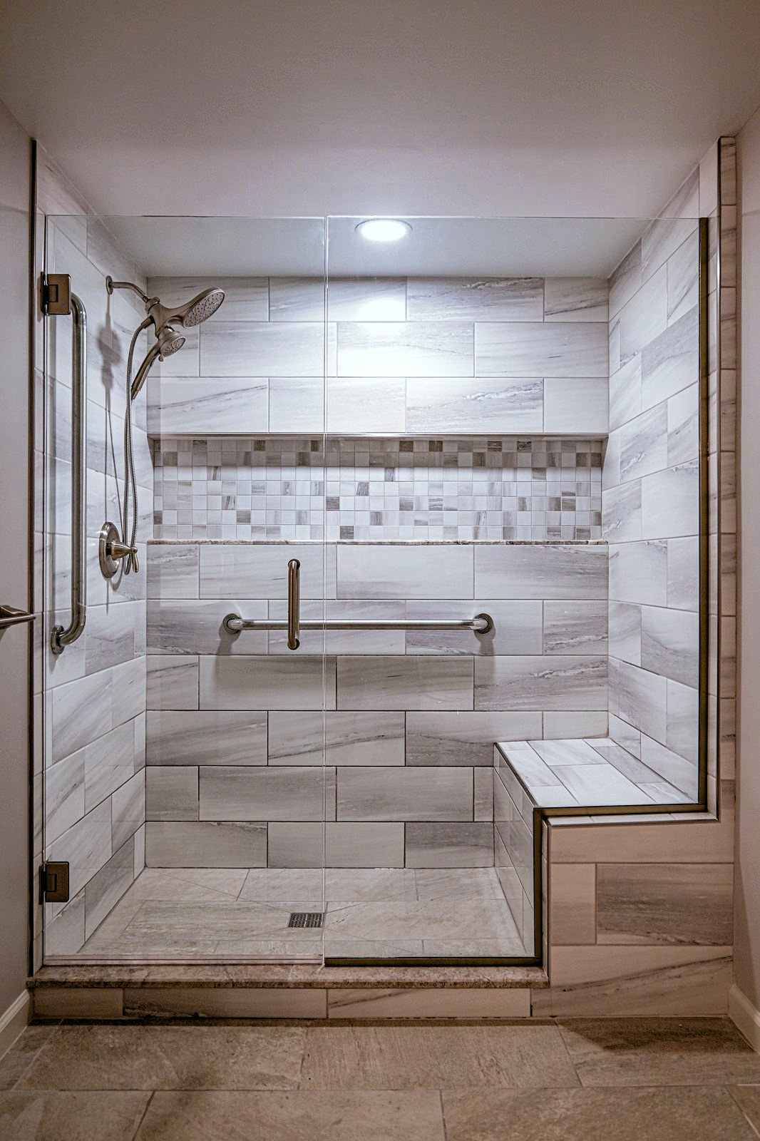 Walk-in shower in Plymouth with a tiled corner bench, mosaic accent band and grab bars