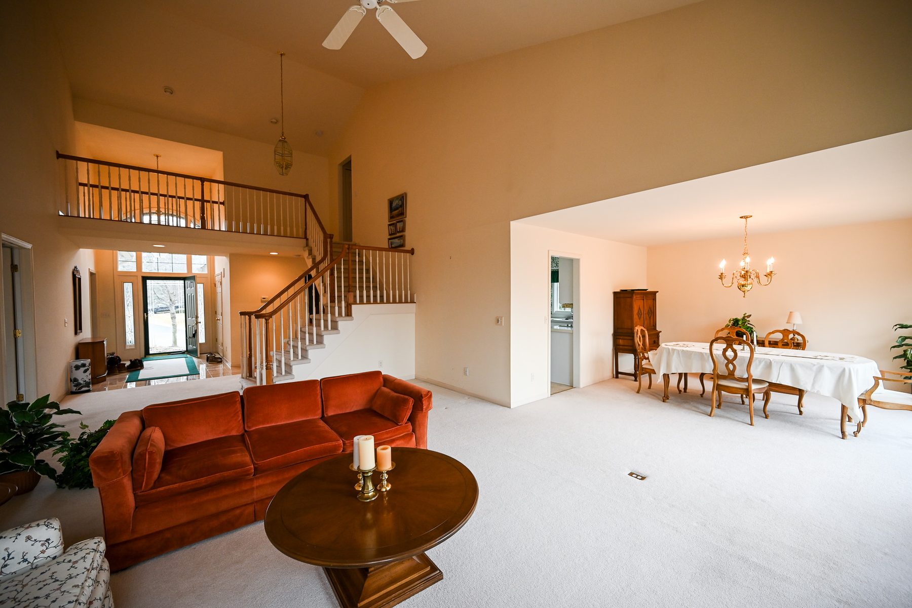 Great room before remodeling, with wall to wall carpet, oak and white spindle railings and a brass chandelier in the two-story foyer