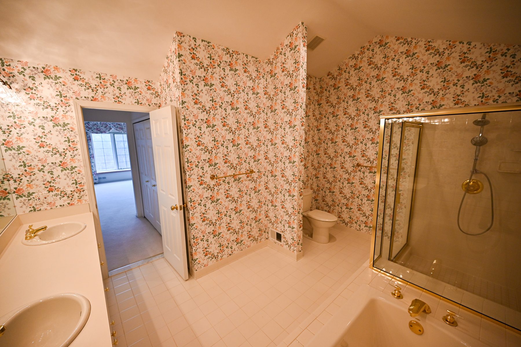Master bathroom before renovation, with floral wallpaper, a drop-in tub and a brass framed shower enclosure
