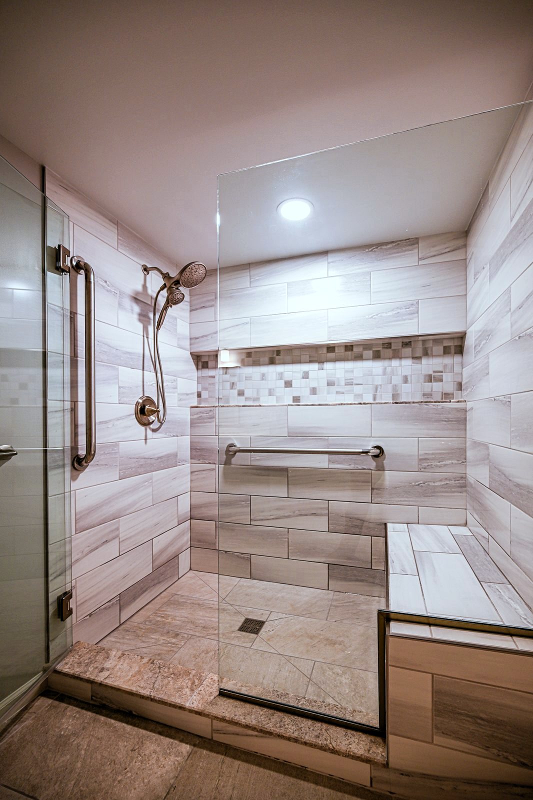 Walk-in shower with a tiled bench, two shower heads and grab bars in a remodeled Plymouth basement bathroom