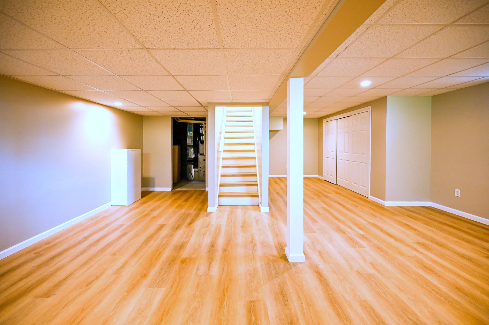 Open refinished basement room in Ypsilanti with stairs, closet wall and warm plank flooring