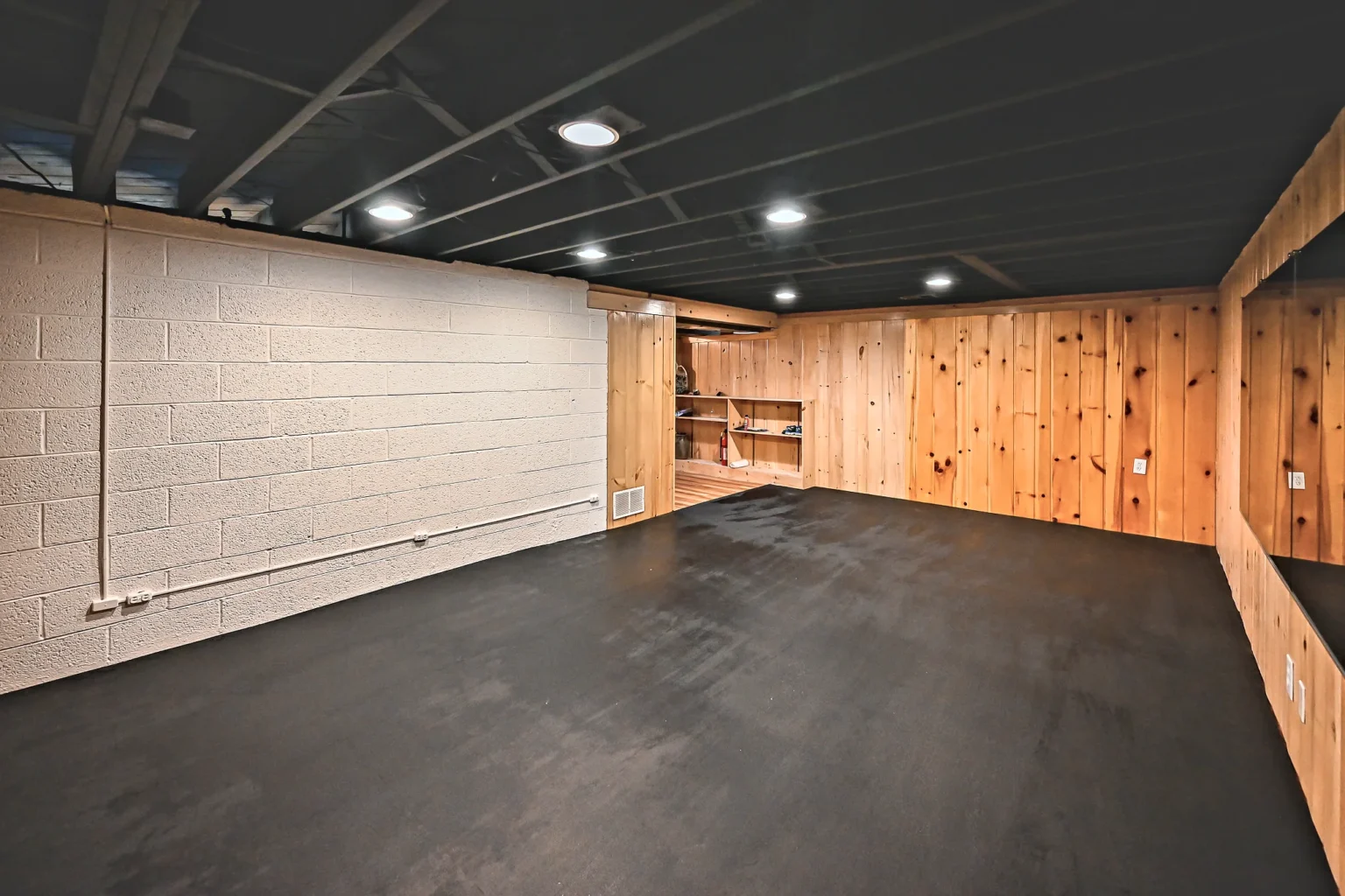 Finished basement home gym in Ann Arbor with a matte black sprayed ceiling, recessed LED lights, black rubber mats and painted block walls