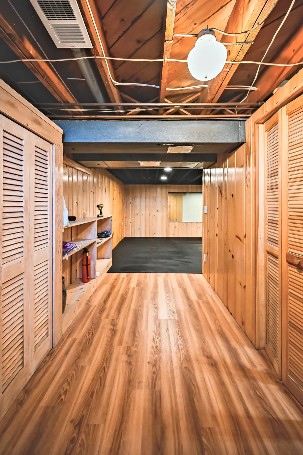 Basement walkway with knotty pine walls, louvered closet doors and new vinyl plank flooring leading to the gym