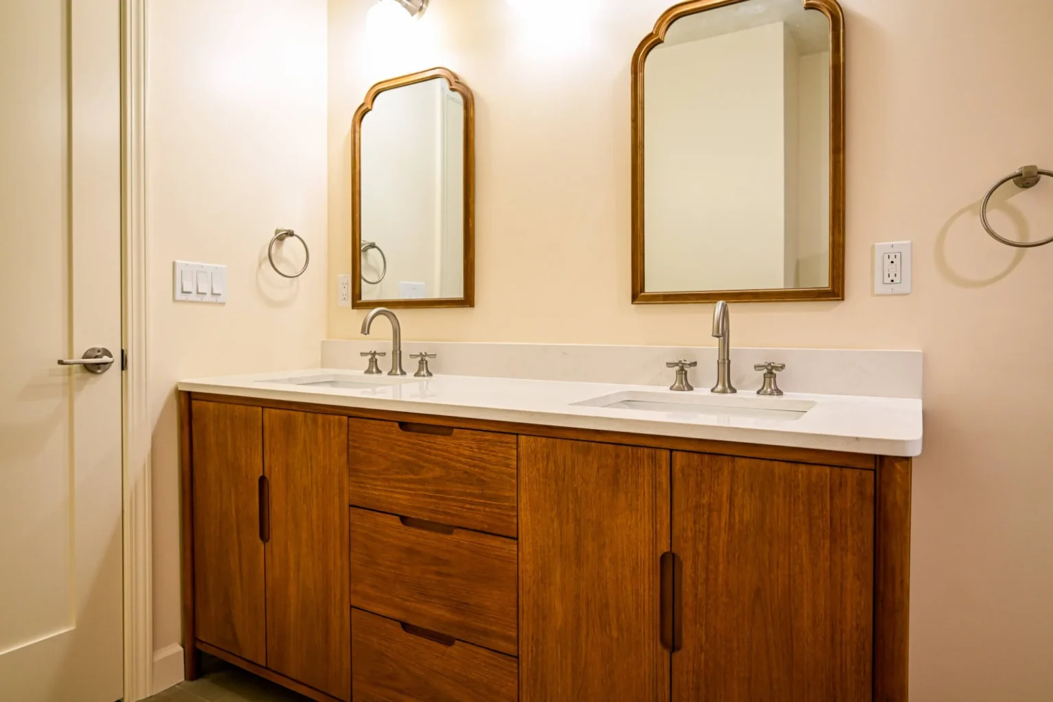 Angled view of a walnut double vanity with three center drawers, white quartz counter and arched wood-framed mirrors in an Ann Arbor bathroom