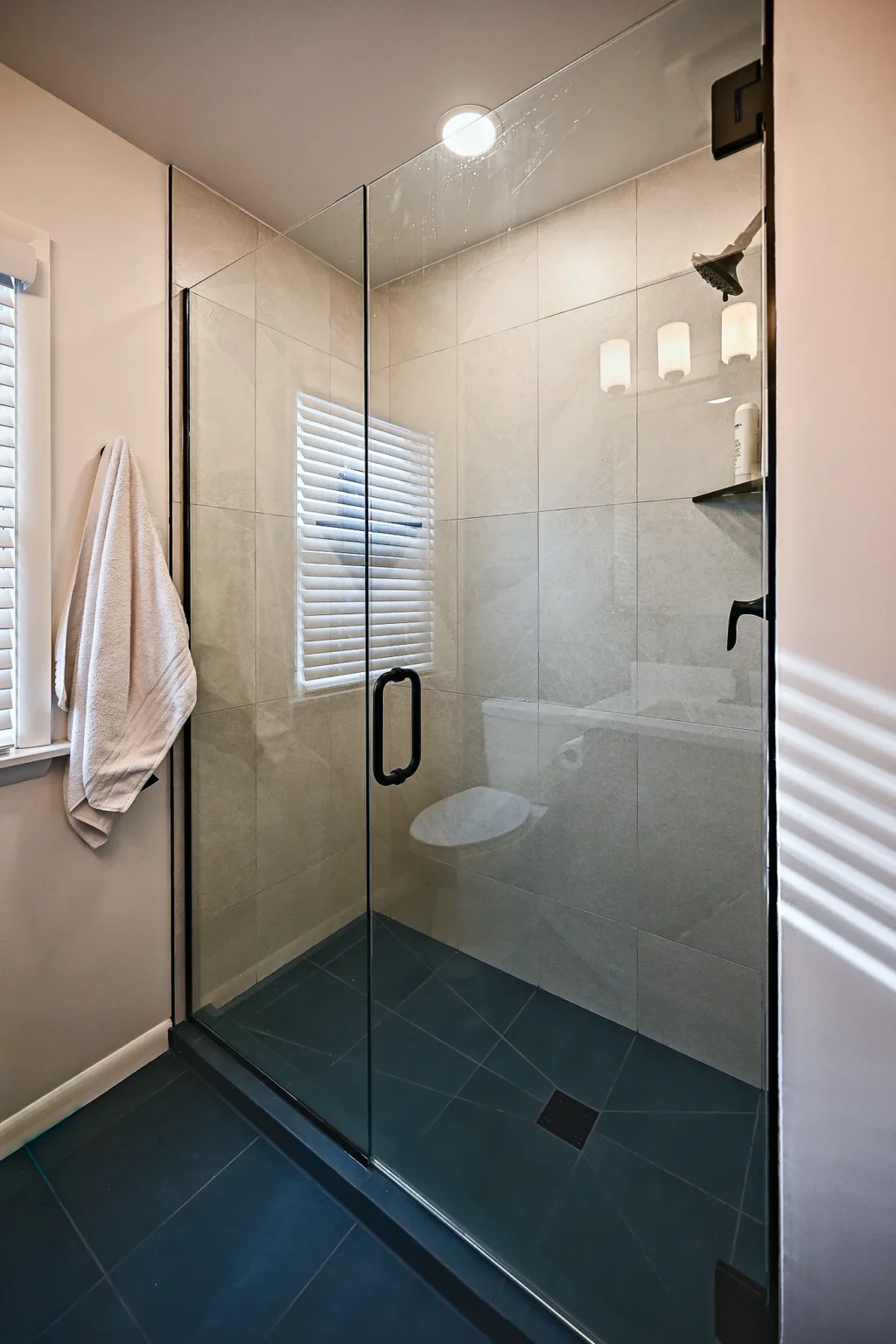 Walk-in shower with a frameless glass panel, matte black hardware, cream porcelain wall tile and a charcoal tile floor