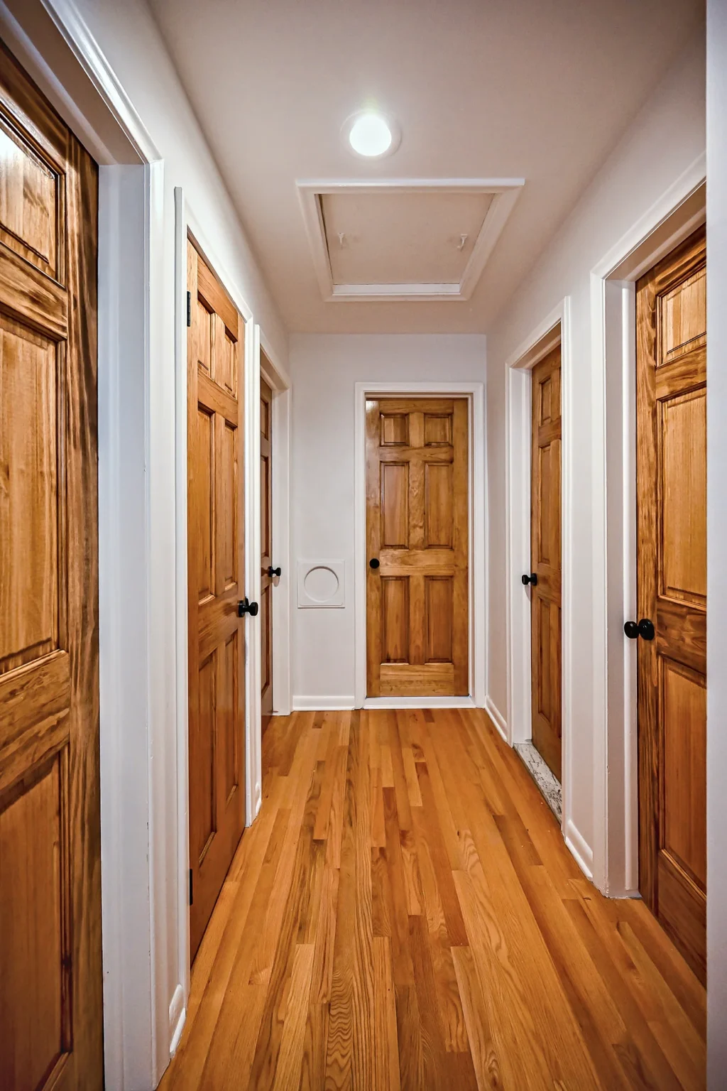 Hallway with warm wood six-panel doors, hardwood flooring and a recessed ceiling light