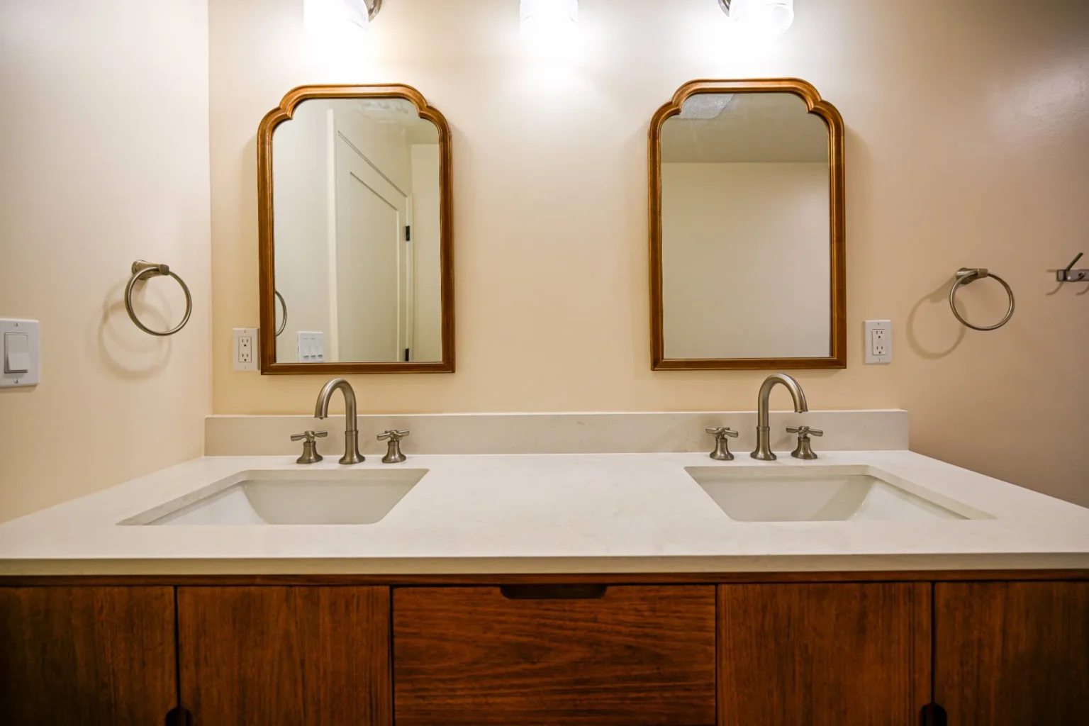Remodeled primary bathroom in Ann Arbor with a walnut double vanity, white quartz top, brushed nickel cross-handle faucets and two arched wood mirrors